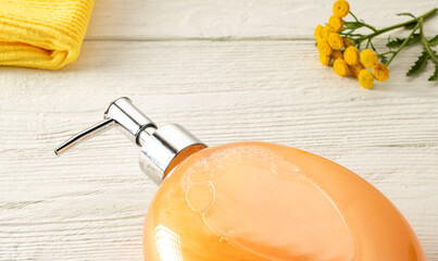 Shampoo bottle, napkin and bright tansy flower on white wooden table