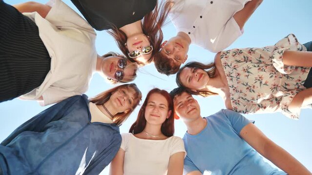 Seven young high school students amicably put their heads together and look down waving their arms.
