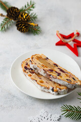 Christmas sweets, slices of stollen with marzipan and dried fruits on a white plate on a light concrete background in Christmas style. Merry Christmas concept