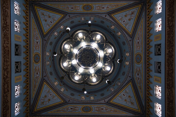 Looking up at the ceiling of a mosque, a chandelier is in the perfect center, surrounded by the...