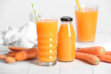 Glasses and bottle of fresh carrot juice on white tile table