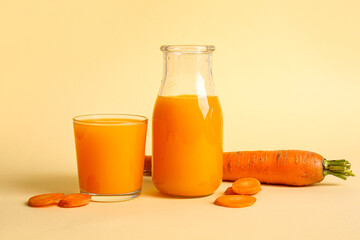 Bottle and glass of fresh carrot juice on orange background