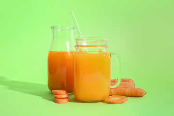 Mason jar and bottle of fresh carrot juice on green background