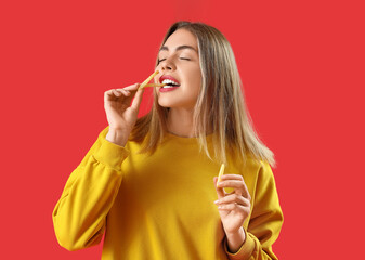 Beautiful young woman eating french fries on red background