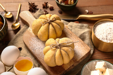Board with pumpkin shaped buns and ingredients on wooden background