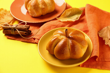 Naklejka na ściany i meble Plates with tasty pumpkin shaped buns on yellow background