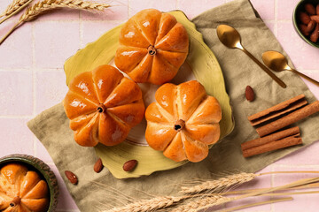 Plate with tasty pumpkin shaped buns on pink tile background