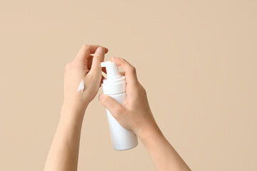 Woman with cosmetic bottle on beige background