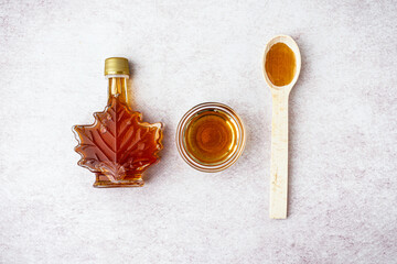 Bottle, bowl and spoon of tasty maple syrup on light background