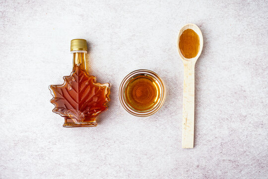 Bottle, bowl and spoon of tasty maple syrup on light background