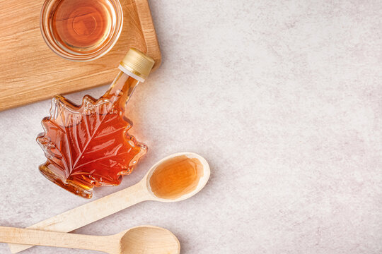 Bottle, bowl and spoons of tasty maple syrup on light background