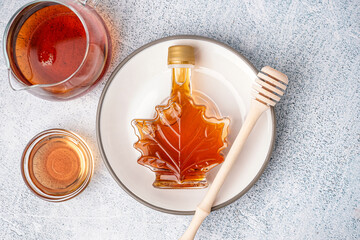 Bottle, bowl and jug of tasty maple syrup on grey background