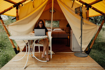 Cute happy freelancer girl using laptop on a sunny day away from the city on a campsite with free...