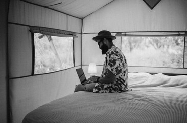 Cute happy freelancer guy using laptop on a sunny day away from the city on a campsite with free wifi. Lifestyle concept. Stay connected. Remote work in nature