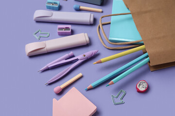 Shopping bag with different school stationery on purple background, closeup