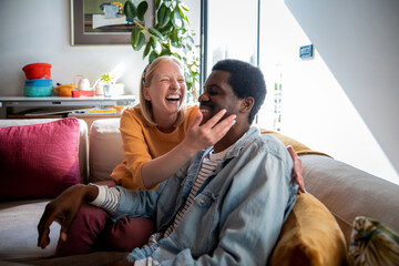 Young interracial couple sitting together on a couch and talking in the living room at home