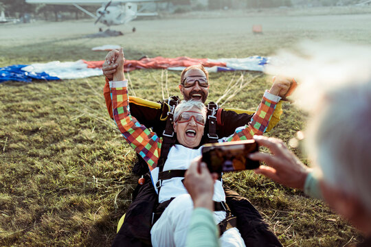 Senior man taking a picture of his wife after landing from a skydive with her instructor