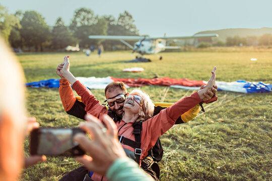 Senior man taking a picture of his wife after landing from a skydive with her instructor