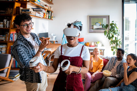 Young and diverse group of friends using a vr headset to play games together in the living room of their flatshare apartment