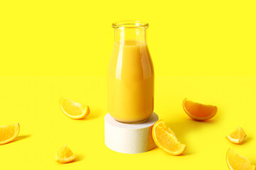 Decorative podium with bottle of fresh orange juice on yellow background