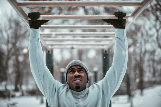 Young athletic and fit african man doing pull ups and chin ups in his workout in a park during winter and snow
