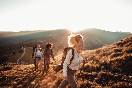 Young and diverse group of female friends hiking in the mountains and looking at the sun setting behind a nearby hill