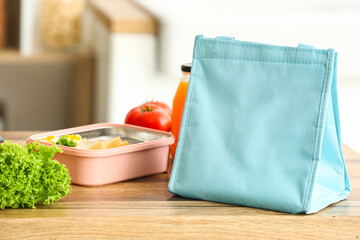 Bag, lunchbox with delicious food and bottle of juice on table in kitchen