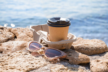 Holder with sunglasses and takeaway cup of hot coffee on beach