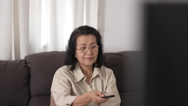 Senior woman holding remote control watching tv at home, recreation and entertainment