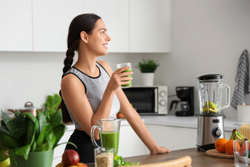Sporty young woman with healthy smoothie in kitchen