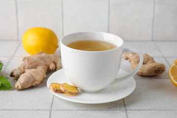 Cup of ginger tea with lemon on white tile background