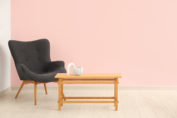 Wooden coffee table with decor and grey armchair near pink wall