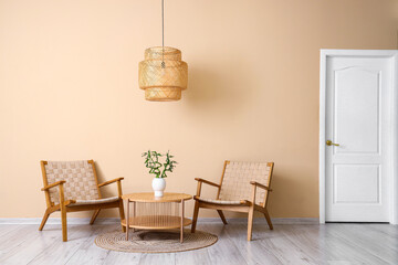 Stylish wicker armchairs, lamp and coffee table near beige wall