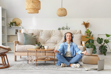 Young woman with headphones meditating on carpet in living room