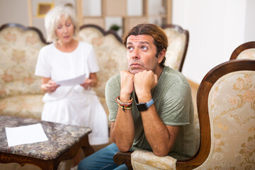 Mature couple fighting over papers at home, adult man ignoring woman
