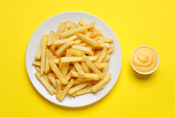 Plate with golden french fries and cheese sauce on yellow background