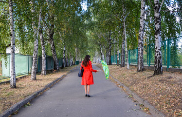 Beautiful brunette girl in red coat with bright umbrella in autumn park standing back and looking into the distance 