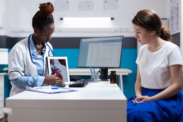 Cardiac doctor specialist showing heart chart on tablet to patient during checkup appointment....