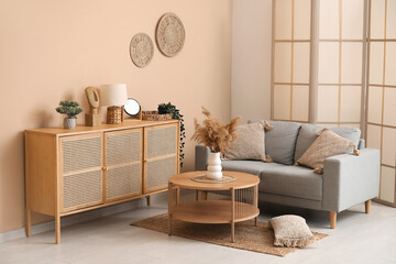 Interior of living room with wicker rug, pampas grass on coffee table and grey sofa