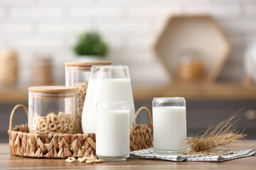 Glasses and jug of fresh milk with cereal rings on wooden table in kitchen