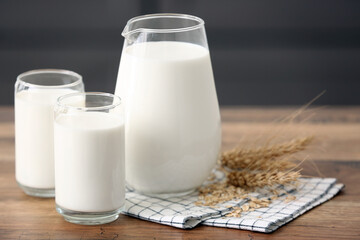 Glasses and jug of fresh milk with wheat ears on wooden table