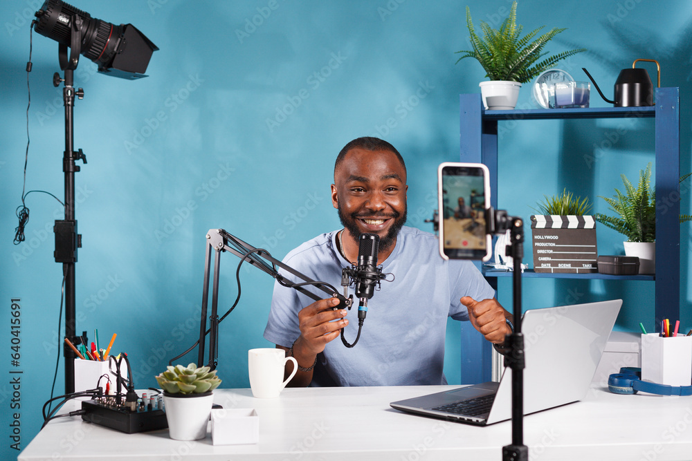 Poster smiling internet streamer speaking in microphone and looking at smartphone camera while filming vide