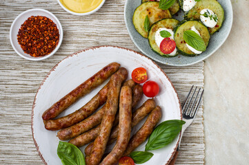 Grilled sausages on a plate with vegetables, herbs, sauce and mustard, top view, horizontal, close.