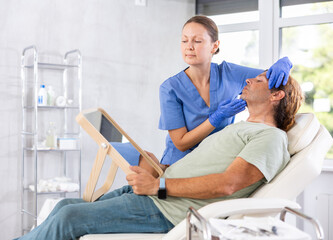 Beautician talking with patient before injection treatment, while client observing herself in mirror.