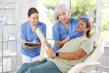 Plastic surgeon preparing patient for botulinum toxin injection treatment on face, while client observing herself in mirror.