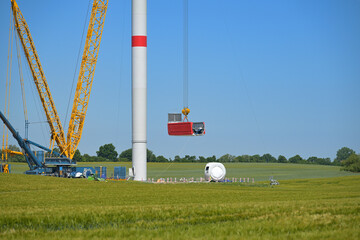 Construction site of a wind turbine, crane lifting the nacelle to install it onto the tower, renewable energy and power concept, blue sky - obrazy, fototapety, plakaty