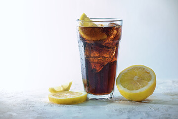 Fresh cola with ice cubes and lemon slices in a drinking glass against a light blue gray background, refreshing sweet caffeine drink, copy space, selected focus