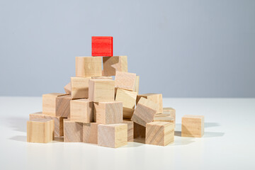 Red cube on the top of a heap from light wooden cubes, concept for business, career, and success, gray background with copy space
