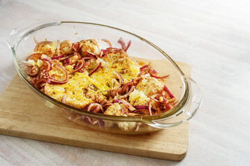 Spicy baked cauliflower steaks with red onions in a glass casserole on a wooden kitchen board on a light table, vegetarian vegetable meal, copy space, selected focus