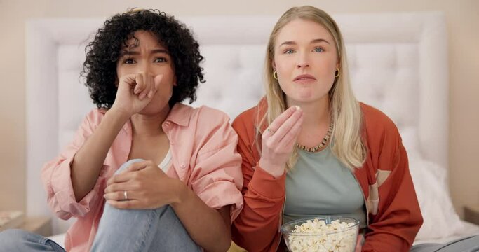 Scary, movie and women friends on bed watching tv with popcorn for horror, terror or thriller at home. Television, face and ladies in bedroom for spooky film, series or streaming serial killer video